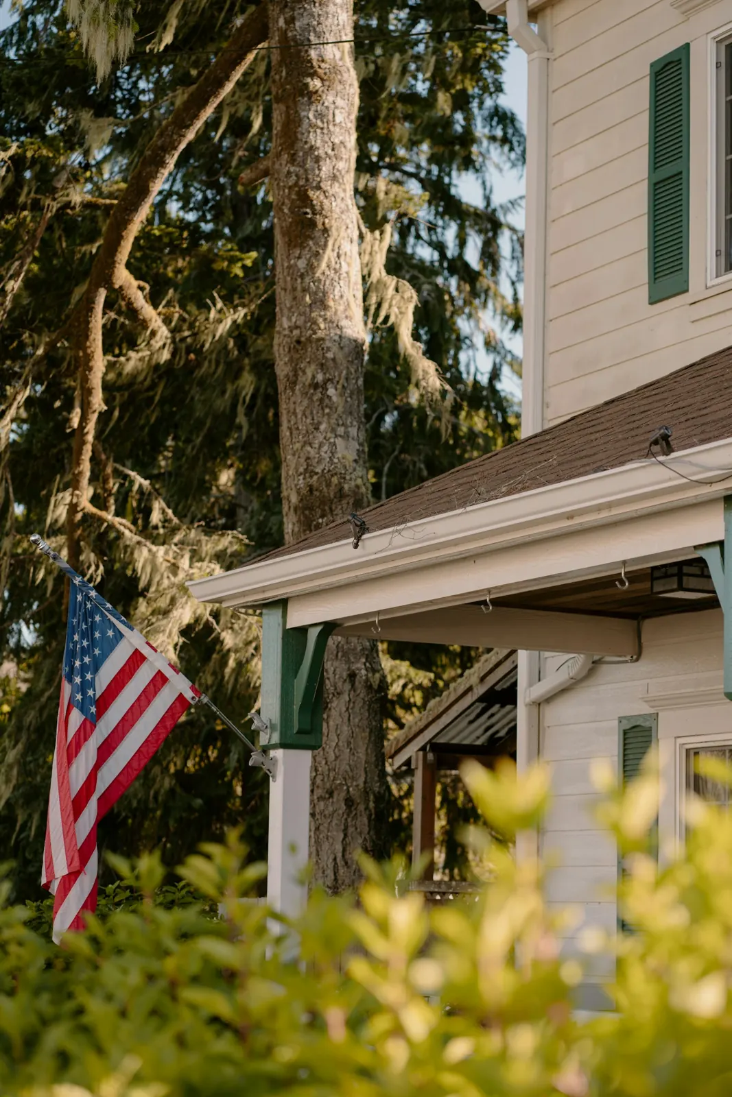An American flag hanging from a house with green shutters